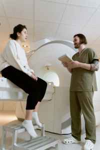Woman sits on an MRI machine talking to a technician in scrubs