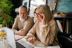 Older couple look at laptop computer screen in home office