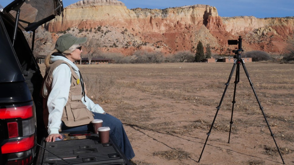 Shelley Carney sits on truck tailgate looking at a camera and mountains