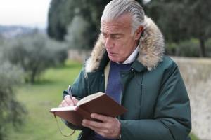 Older man outdoors wearing a coat writes in a journal